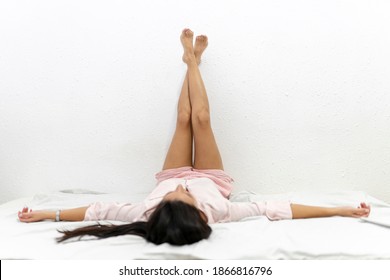 Beautiful Young Long Haired Woman With Legs Up On The Wall Lying On Bed With Outstratched Arms, Copy Space