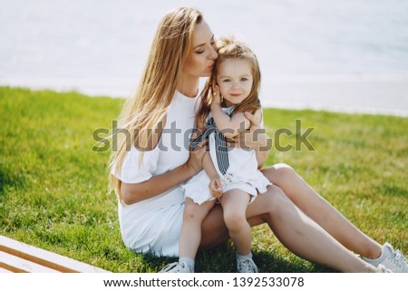 a beautiful young long-haired mom sitting in the park with her beautiful little daughter