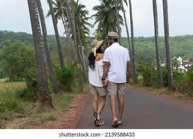 A beautiful young lovely attractive couple looking at each other, embracing, making love, smiling, cuddling walking on a famous Parra Coconut road in Goa surrounded by or lined with palm trees fields.