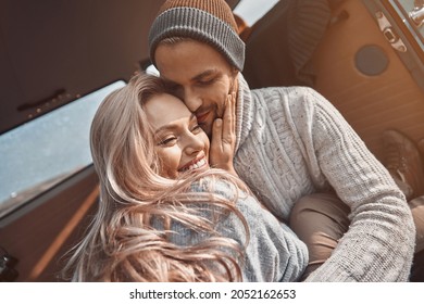 Beautiful young loving couple embracing and smiling while spending time in their minivan