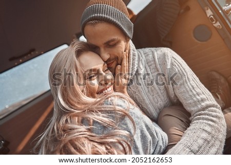 Beautiful young loving couple embracing and smiling while spending time in their minivan