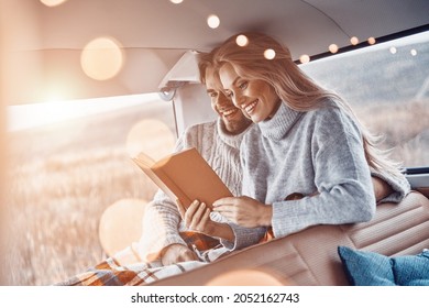 Beautiful young loving couple reading book together and smiling while spending time in their minivan - Shutterstock ID 2052162743
