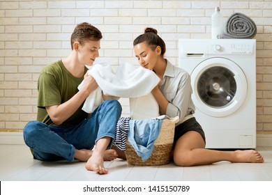 Beautiful Young Loving Couple Is Smiling While Doing Laundry At Home.