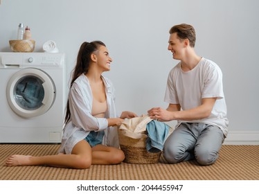 Beautiful Young Loving Couple Is Smiling While Doing Laundry At Home.