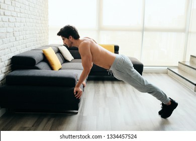 Beautiful Young Man Training And Working Out. Athlete Exercising With A Chest Routine For Wellness In His Living Room. Latino People Doing Push-ups With Backward Grip Using Sofa At Home.