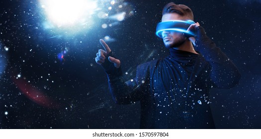 Beautiful young man using VR helmet while touching air in colorful neon lights. Guy in glasses of virtual reality with blue backlight over dark magic universe background.  - Powered by Shutterstock