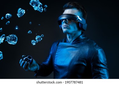 Beautiful young man using VR helmet with futuristic gadgetin hand. Blue neon lights. Guy in glasses of virtual reality with blue backlight over dark magic background. - Powered by Shutterstock