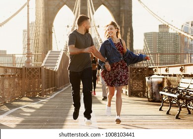 Beautiful young man and woman pose on the Brooklyn Bridge in the rays of morning sun