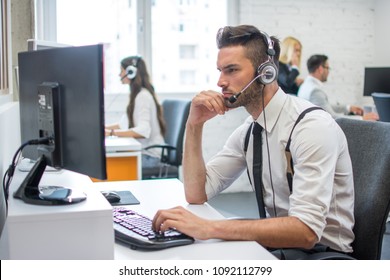 Beautiful young man working in call center. Customer support operator with headset working in office with his colleagues.