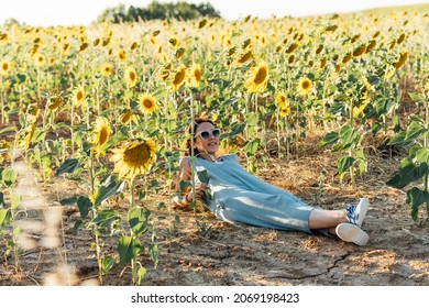 Beautiful Young Middle-aged Woman Lying In A Field Of Sunflowers Wearing Sunglasses. Rural Tourism. Healthy Life Style.