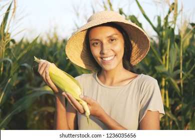 Beautiful Young Mixed Race Farmer Woman in Hat with Ripe Corn at Organic Farm Field. Woman Smiling and Showing Thumb Up at Camera in Natural Sunset Light. 4K, Slowmotion Agricultural Harvest Footage.