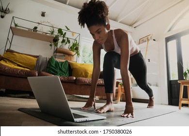 Beautiful young mixed race woman working out from home, online workout on laptop