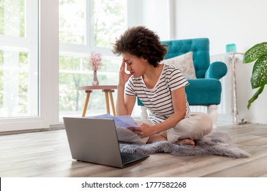 Beautiful Young Mixed Race Woman Sitting On The Living Room Floor, Calculating Bank Loan Payout Rates And Paying Household Bills, Anxious And Worried