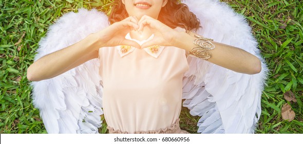 Beautiful young model with angel wings on the grasses background.
Girl model wearing a white dress with angel wings and posting hands to heart shape.