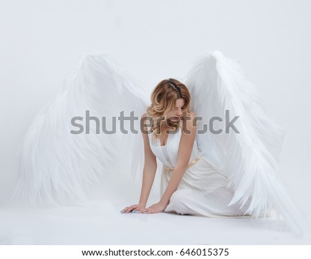 beautiful young model with big angel wings sitting in the studio. white background.