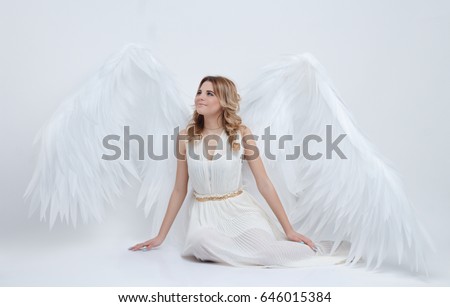 beautiful young model with big angel wings sitting in the studio and looking up. white background.