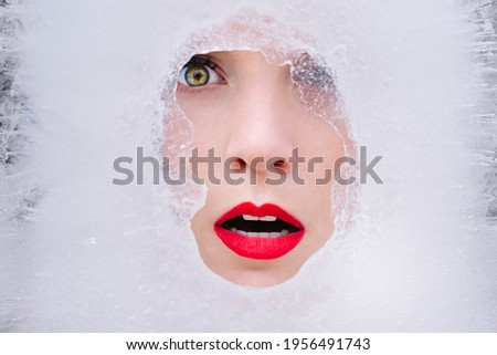 Beautiful young model face in ice. Cold frozen winter beauty with red lips in ice cube. Fashion art woman portrait.