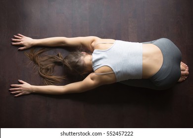 Beautiful Young Model Girl Working Out At Home, Doing Yoga Exercise For Spine On Wooden Floor, Lying In Child Pose, Balasana Posture, Resting After Practice. Full Length, High Angle View