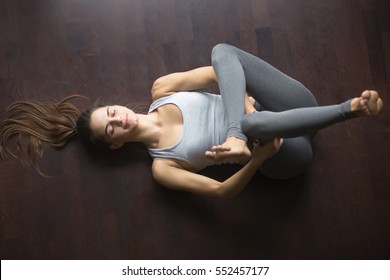 Beautiful Young Model Working Out At Home, Doing Yoga Exercise On Floor, Lying In Eye Of The Needle Hip Stretch Pose (Dead Or Reclining Pigeon Posture), Resting After Practice. Full Length, Top View