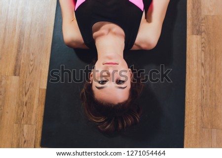 Beautiful young model working out at home, doing yoga exercise on floor, lying in Parivrtta Supta Padangushthasana, reclined variation of Twisting Extended Hand to Big Toe pose. Top view. Full length.
