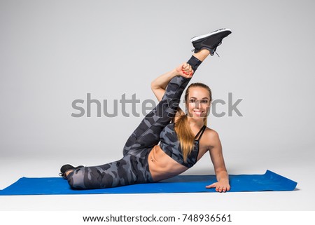 Beautiful young model working out doing stretching exercise on mat on gray. Sport active lifestyle concept.