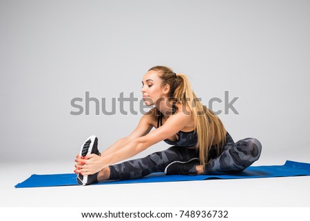 Beautiful young model working out, doing stretching yoga exercise on mat on gray. Sport active lifestyle concept.