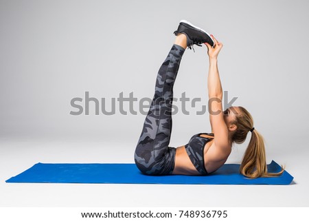 Beautiful young model working out, doing stretching yoga exercise on mat on gray. Sport active lifestyle concept.