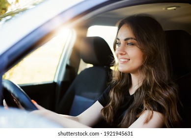 Beautiful Young Modern Girl Driving A Car On Sunny Summer Day. Female Driver Alone In The Car, Close-up, Sun On The Background.