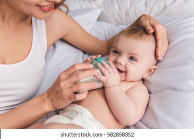 Beautiful Young Mom Is Feeding Her Cute Baby With Baby Bottle And Smiling