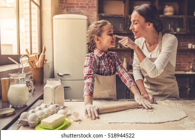 Beautiful young mom and her cute little daughter are playing and smiling while baking in kitchen at home