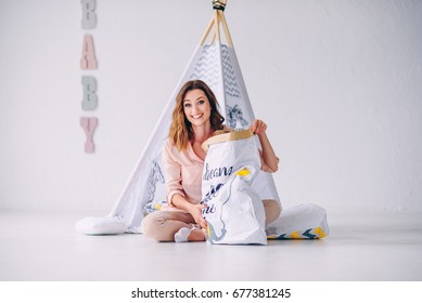 A Beautiful Young Mom And Her Little Son Having Fun In The Light Room. Little Boy Was Hiding In The Paper Eco-bag.