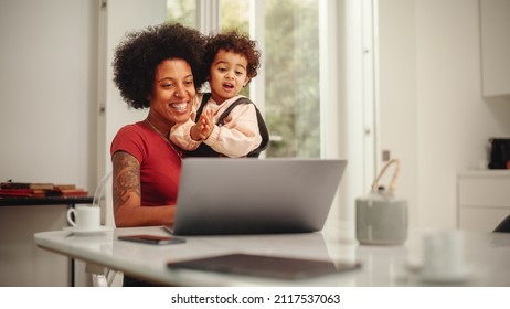 Beautiful Young Mom Holding Her Lovely Baby Son, Using Laptop Computer in Living Room in Apartment. Mother is Working from Home, Online Shopping, Watching Social Media or Writing Emails. - Powered by Shutterstock