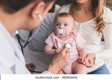 Beautiful young mom is holding her cute baby while doctor is listening to baby's lungs