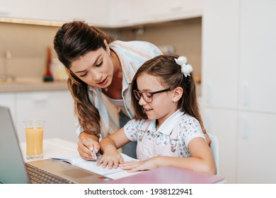 Beautiful young mother helping her younger daughter with homework.