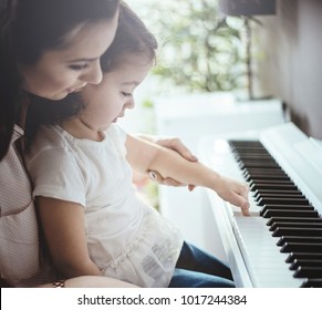 Beautiful young mother with her daughter together, learning playing musical instrument - Powered by Shutterstock