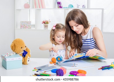 beautiful young mother and her little daughter drawing with crayons on the album. mother and daughter having fun at home.