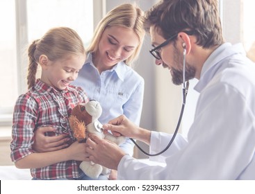 Beautiful young mother and her little daughter at the pediatrician. Doctor is examining little patient using a stethoscope
