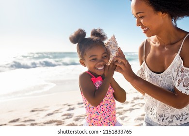Beautiful young mother holding seashell near happy daughter ear at beach while she listening the sound of the ocean. Cute little child hearing to cockleshell with mom at tropical beach with copy space - Shutterstock ID 2151833765