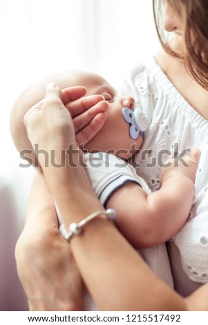 Beautiful young mother holds the baby in her arms. Mom holds the baby's legs in her hands for 3 months. Love. Motherhood. Happiness. House.