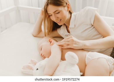 Beautiful young mother kissing her newborn baby sleeping in bed, Health care, mother's day