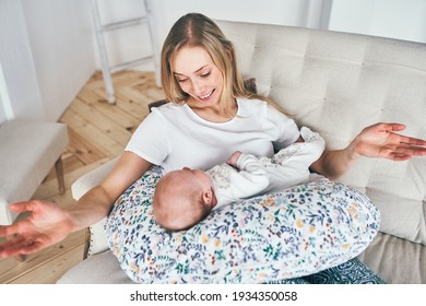 A beautiful young mother with long blonde hair and a daughter of 2-3 months are resting on the bed with blue pillow in the bedroom. Happiness is in children. The long-awaited baby