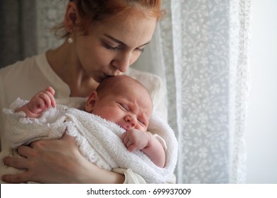 beautiful young mother and newborn baby in her arms standing by the window