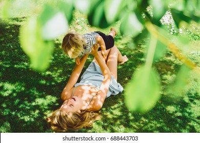 Beautiful Young Mother With A Small Child Draws In The Garden On The Lawn. Mom And Her Son Paint On The Nature.