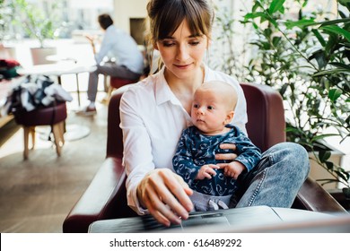 Beautiful young mother working with laptop computer and breastfeeding, holding and nursing her newborn baby at cafe. Mom - business woman feeding newborn.