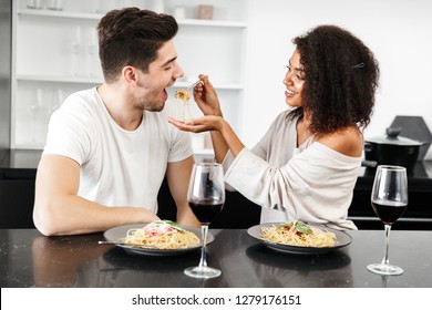 Beautiful Young Multiethnic Couple Having A Romantic Dinner At Home, Drinking Red Wine And Eating Pasta