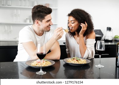 Beautiful Young Multiethnic Couple Having A Romantic Dinner At Home, Drinking Red Wine And Eating Pasta