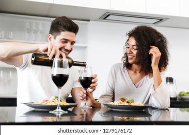 Beautiful young multiethnic couple having a romantic dinner at home, drinking red wine and eating pasta, pouring - Powered by Shutterstock