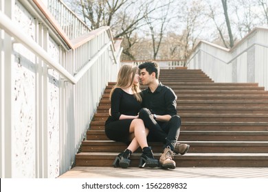 Beautiful young multiracial couple, student couple in love, sit wooden staircase in the city. Beautiful Turkish brunette guy hug a Caucasian girl in black clothing. Date young people in sunny weather. - Powered by Shutterstock