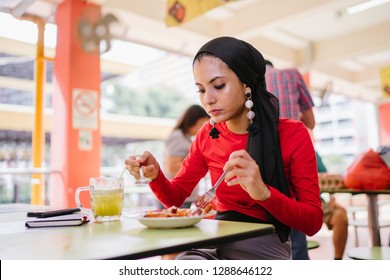 A Beautiful Young Muslim Malay Woman In A Hijab Head Scarf (tudung) Is Eating Her Breakfast Of Halal Nasi Lemak As She Sits In A Food Court During The Day. She Is Beautiful And Attractive. 