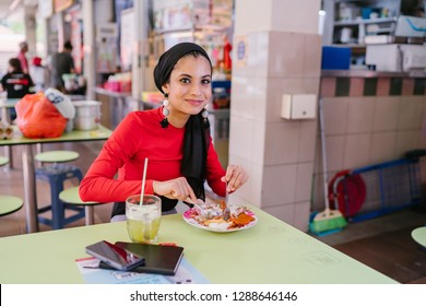 A Beautiful Young Muslim Malay Woman In A Hijab Head Scarf (tudung) Is Eating Her Breakfast Of Halal Nasi Lemak As She Sits In A Food Court During The Day. She Is Beautiful And Attractive. 